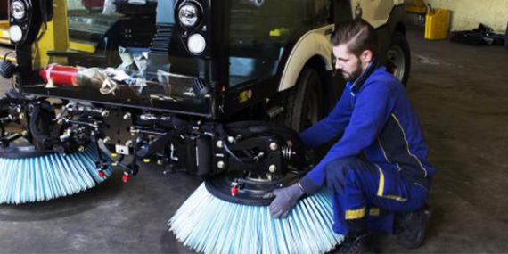 Service engineer fitting a brush to a compact sweeper.